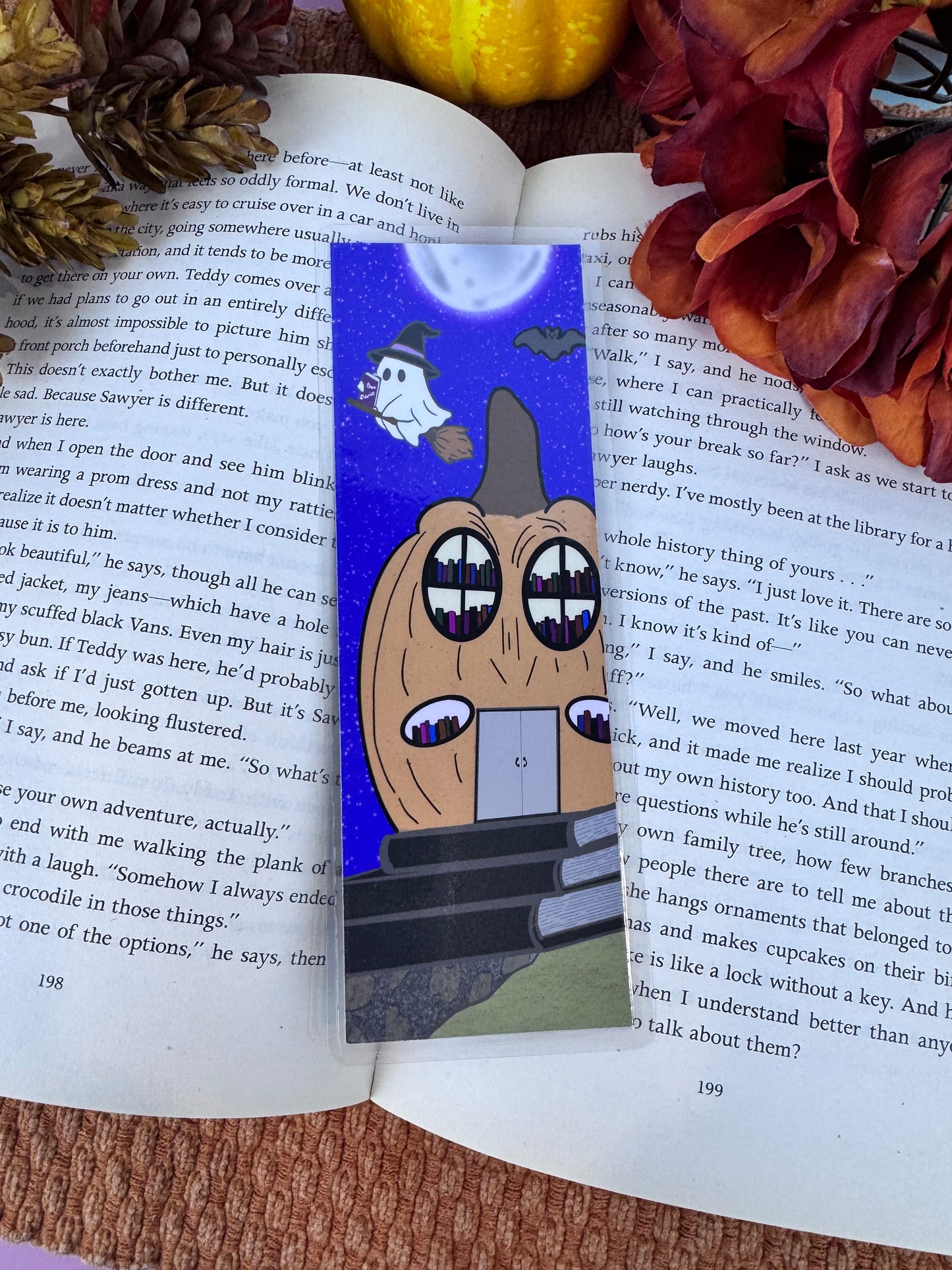 Handmade laminated ghost bookmark featuring a cute ghost on a broomstick leaving a pumpkin library under a full moon — spooky cute design for readers.